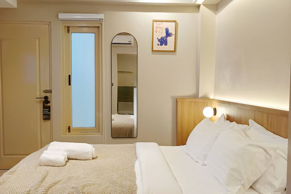 Una habitación de hotel con una cama, una mesita de noche, un espejo y una puerta.