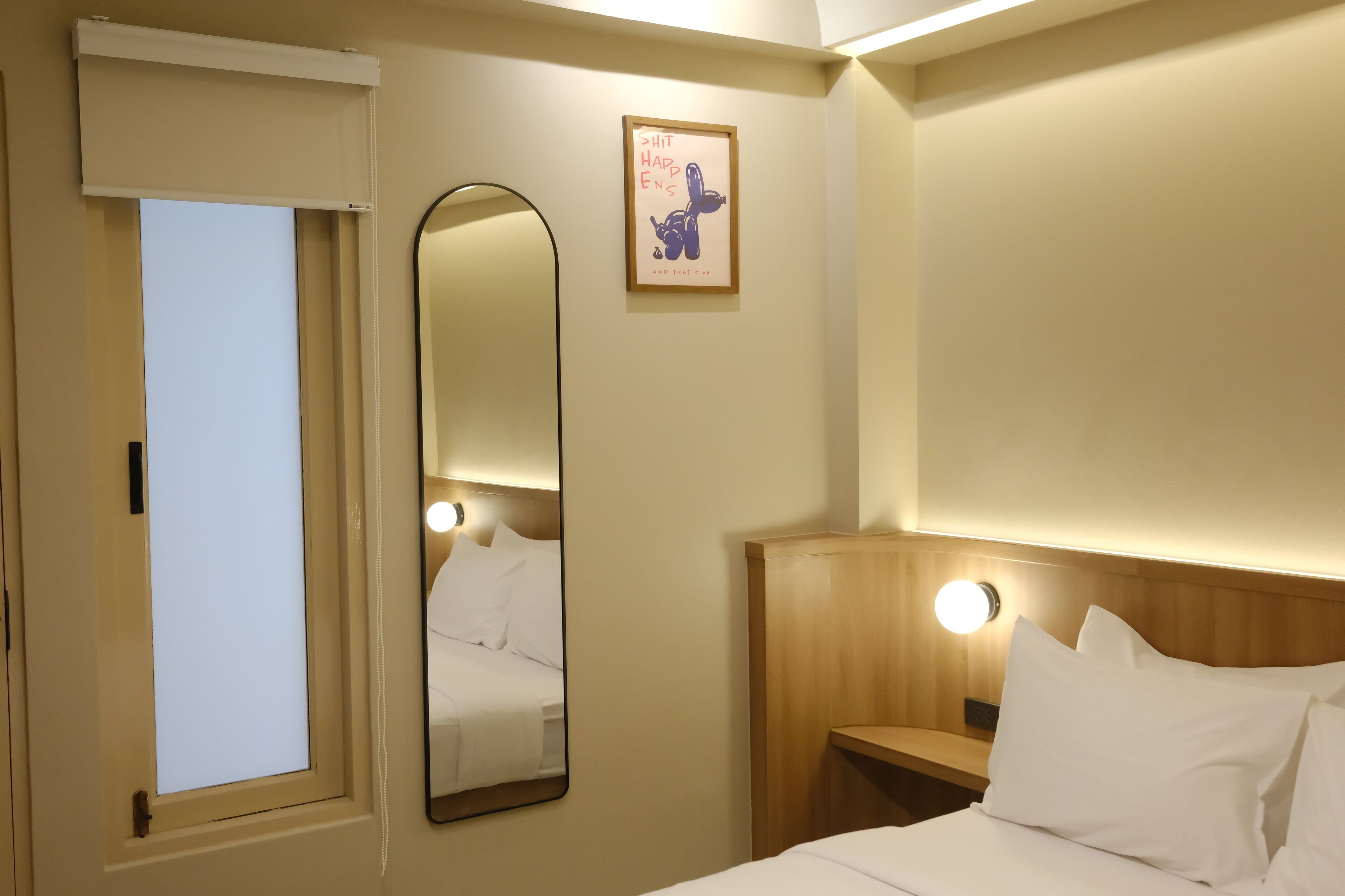Une chambre d’hôtel comprenant un lit, une table de chevet, un miroir, une porte et un luminaire fixé au mur.