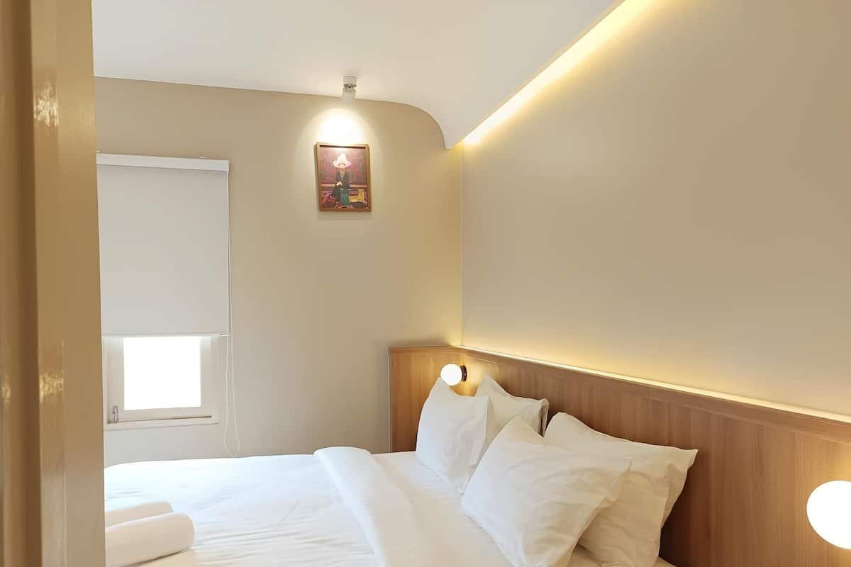 Una cama bien hecha con sábanas blancas, un cabecero de madera y una mesita de noche con una lámpara.