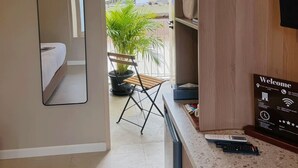 A hotel room with a bed, a small table with a chair, a potted plant, a welcome sign, and a view of the outdoors. - Urban Room Samed (Rayong)