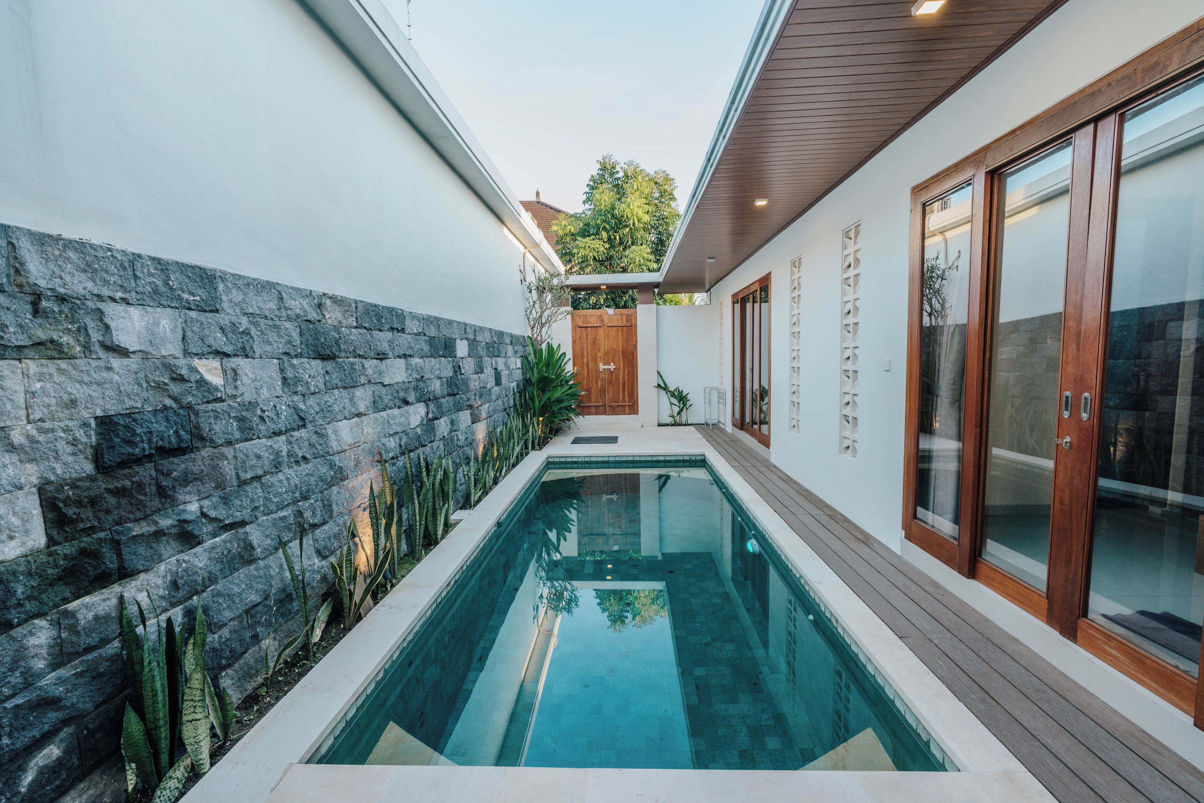 A modern pool area with stone walls and wooden deck.