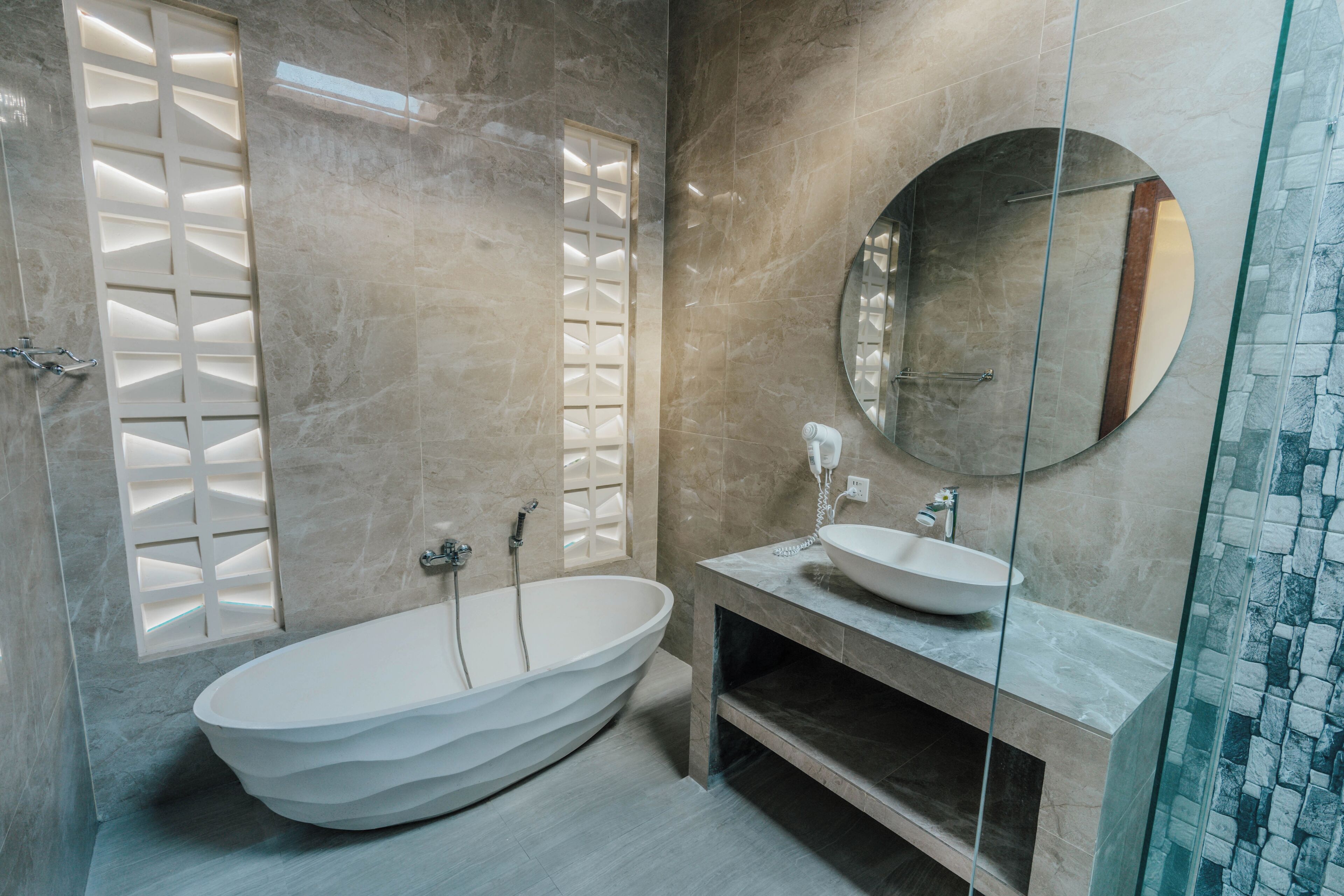 A modern bathroom with a freestanding bathtub, a round mirror, and a glass shower enclosure.