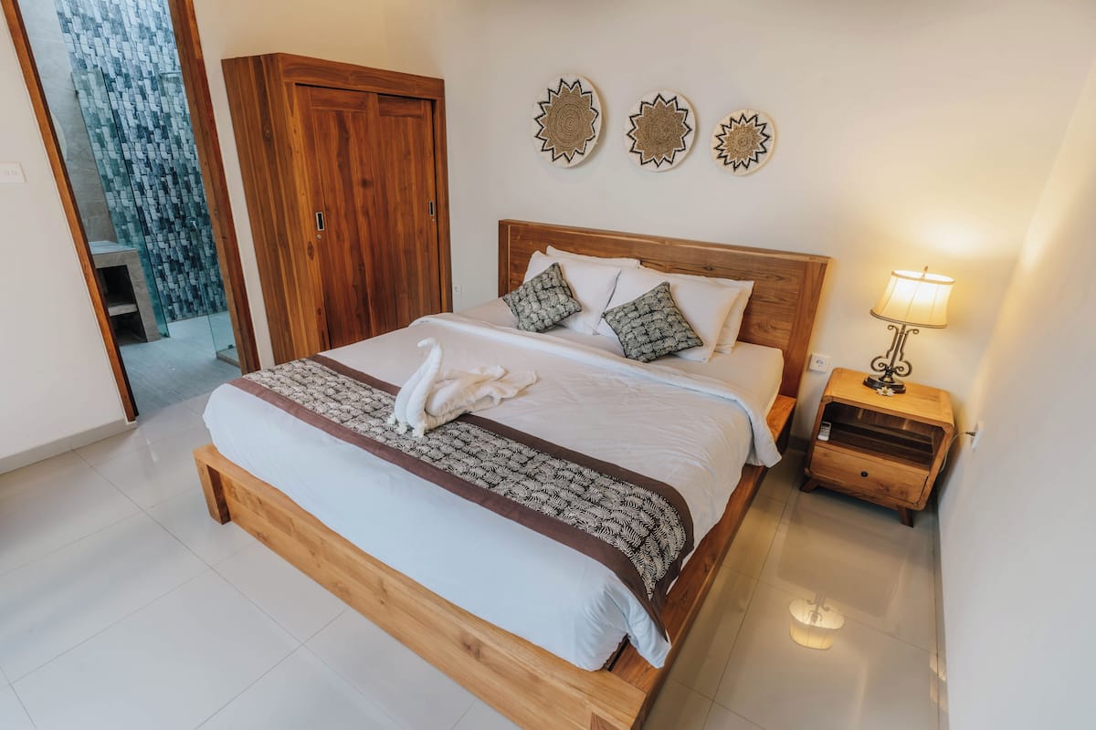 Una cama bien hecha con cabecera marrón, una mesita de noche de madera con lámpara y decoración en la pared.
