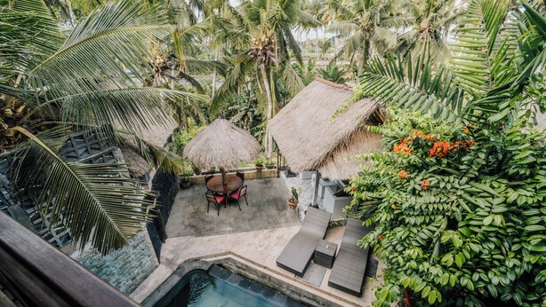 A pool area with lounge chairs and a thatched-roof table, surrounded by lush greenery and palm trees. - Ganesha Villa (Ubud)