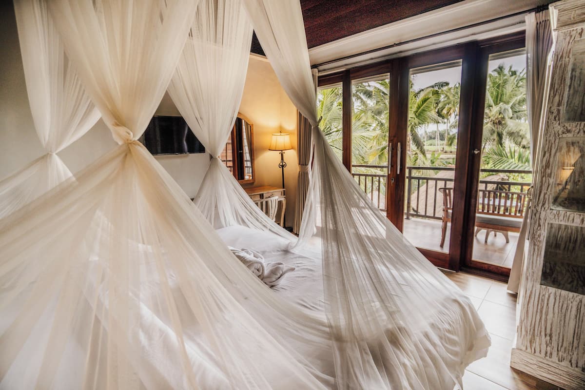 Un dormitorio con cama a dosel, una mesita de noche, una lámpara y vistas al exterior.