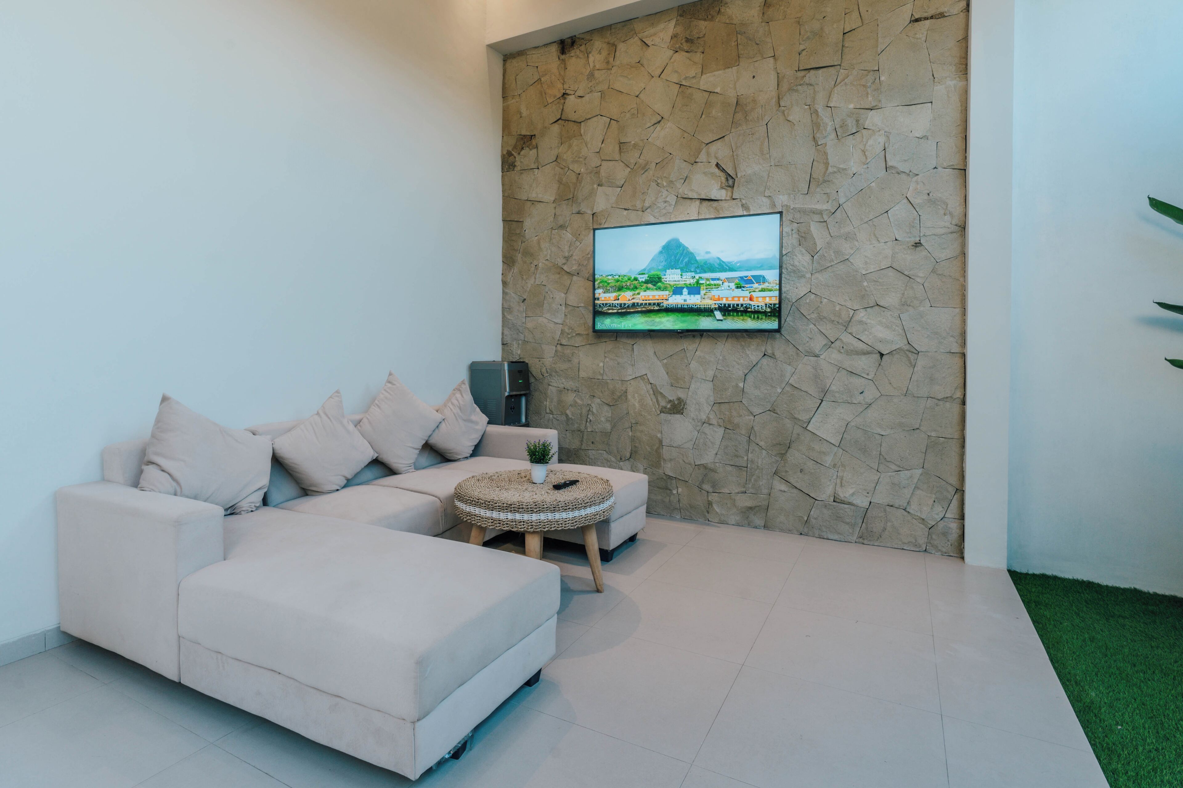 A modern living room with a beige sectional sofa, a small round coffee table, and a flat-screen TV mounted on a stone wall.