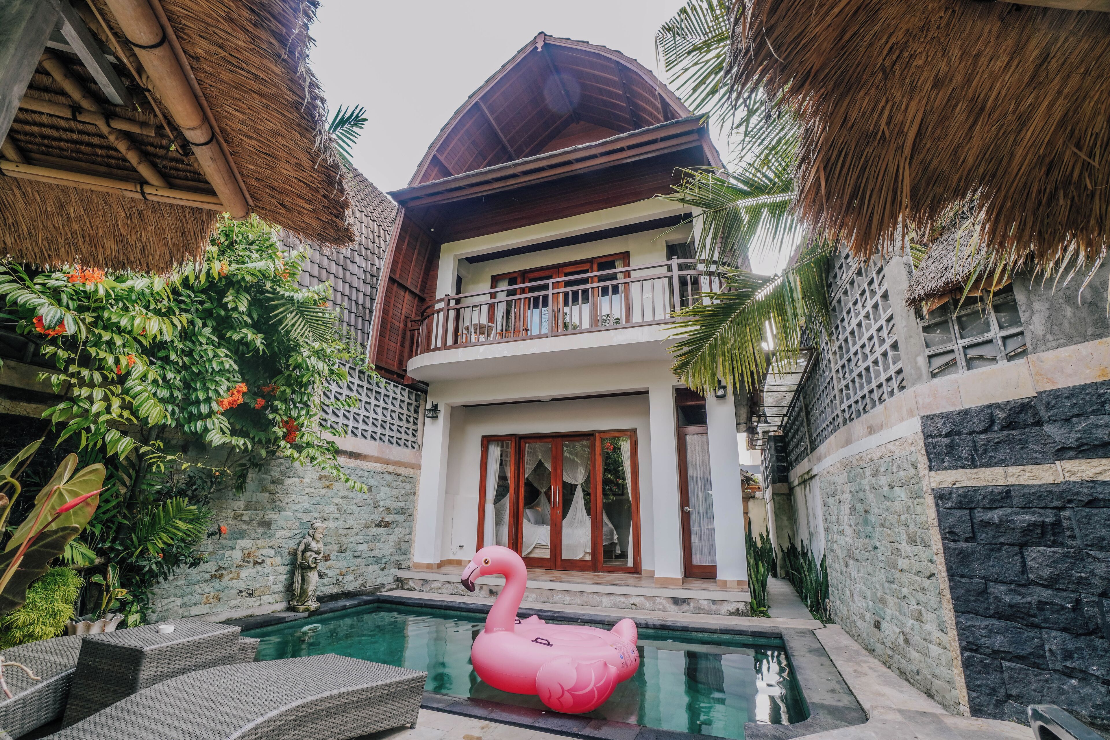 A villa with a swimming pool, a pink flamingo float, and lush greenery.