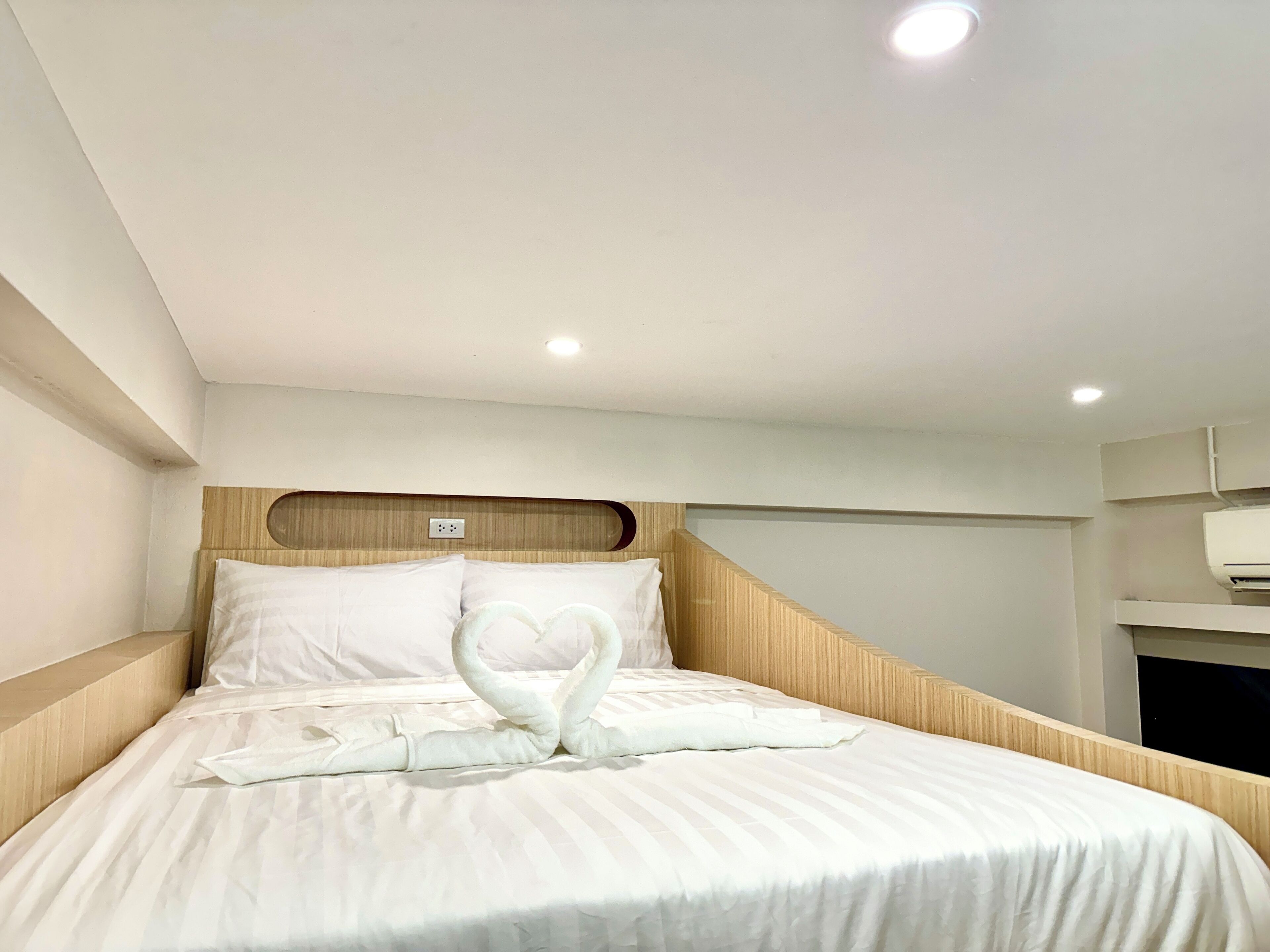 Une chambre d’hôtel avec un lit bien fait, une tête de lit en bois et un climatiseur fixé au mur.