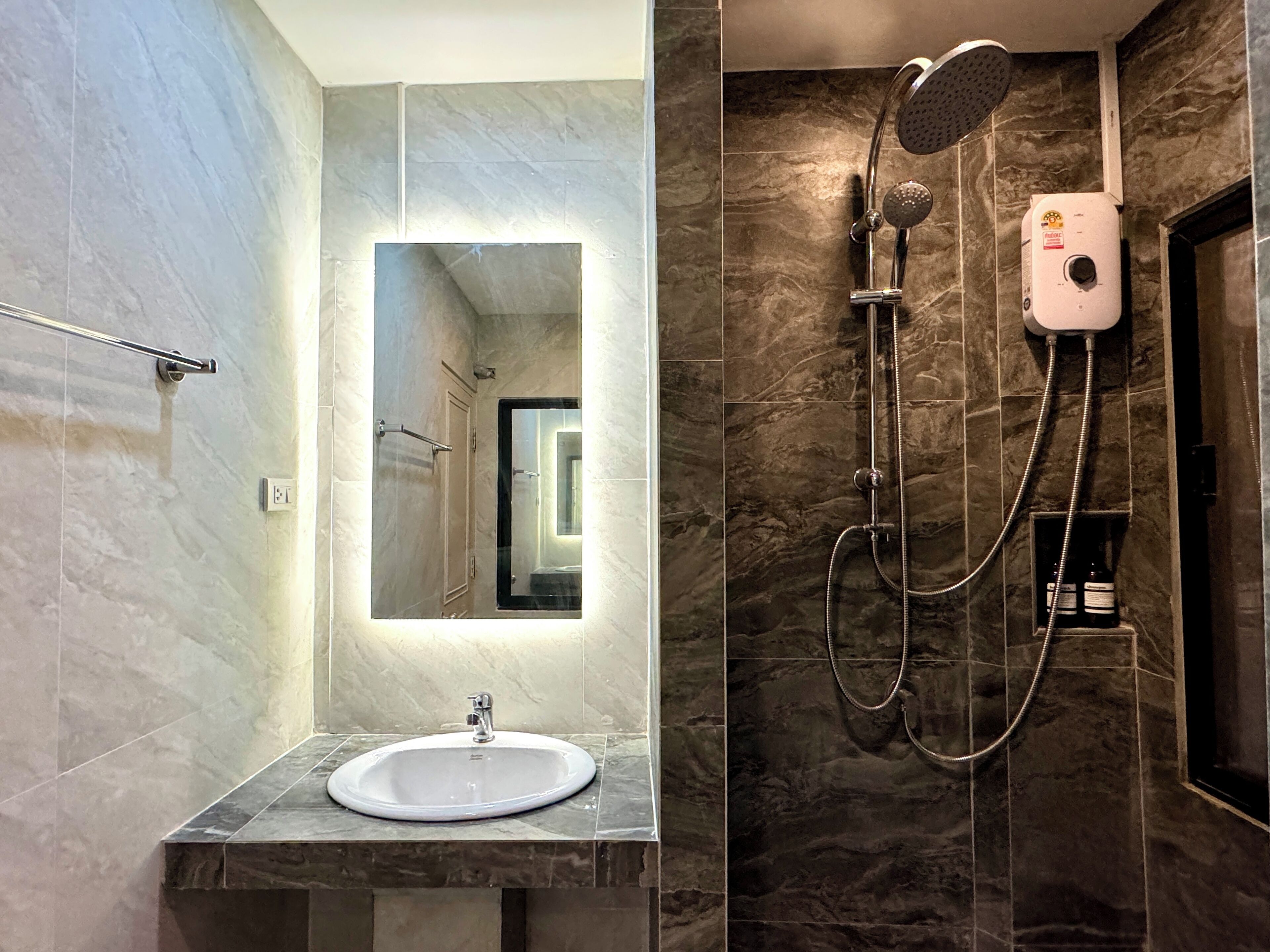A modern bathroom with a marble sink, a large mirror, and a shower with a handheld showerhead.