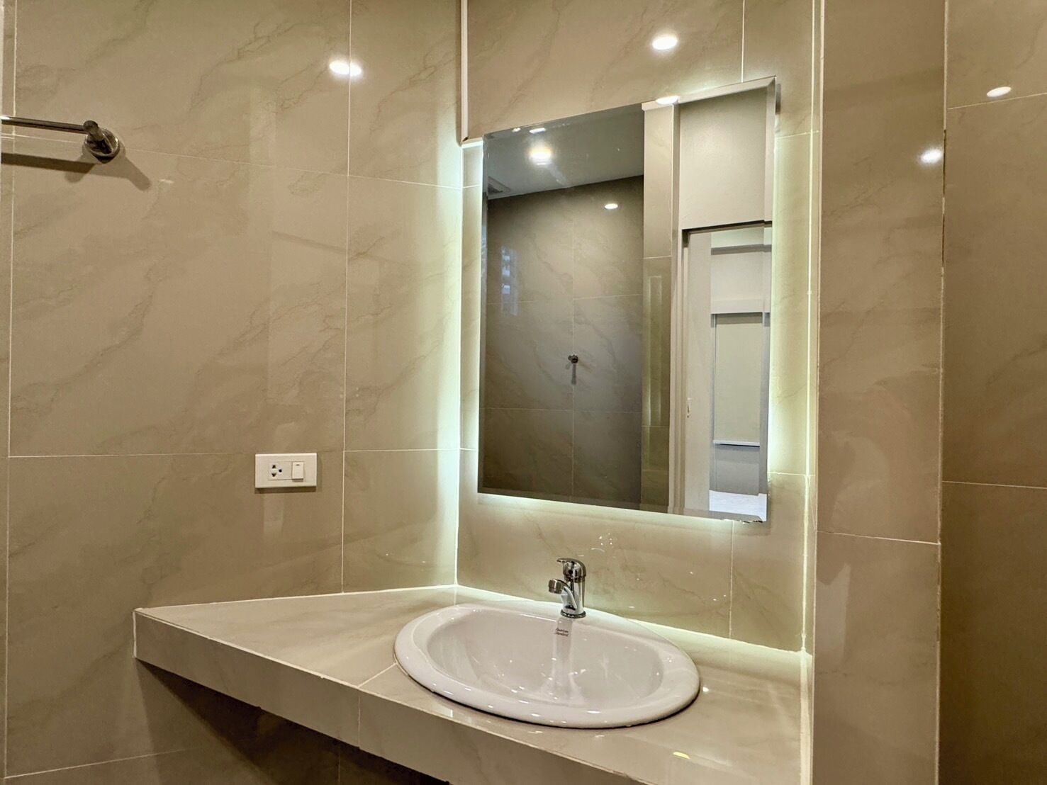 Une salle de bain moderne avec un sol en marbre, un lavabo blanc doté d’un seul robinet et un grand miroir au-dessus du lavabo.