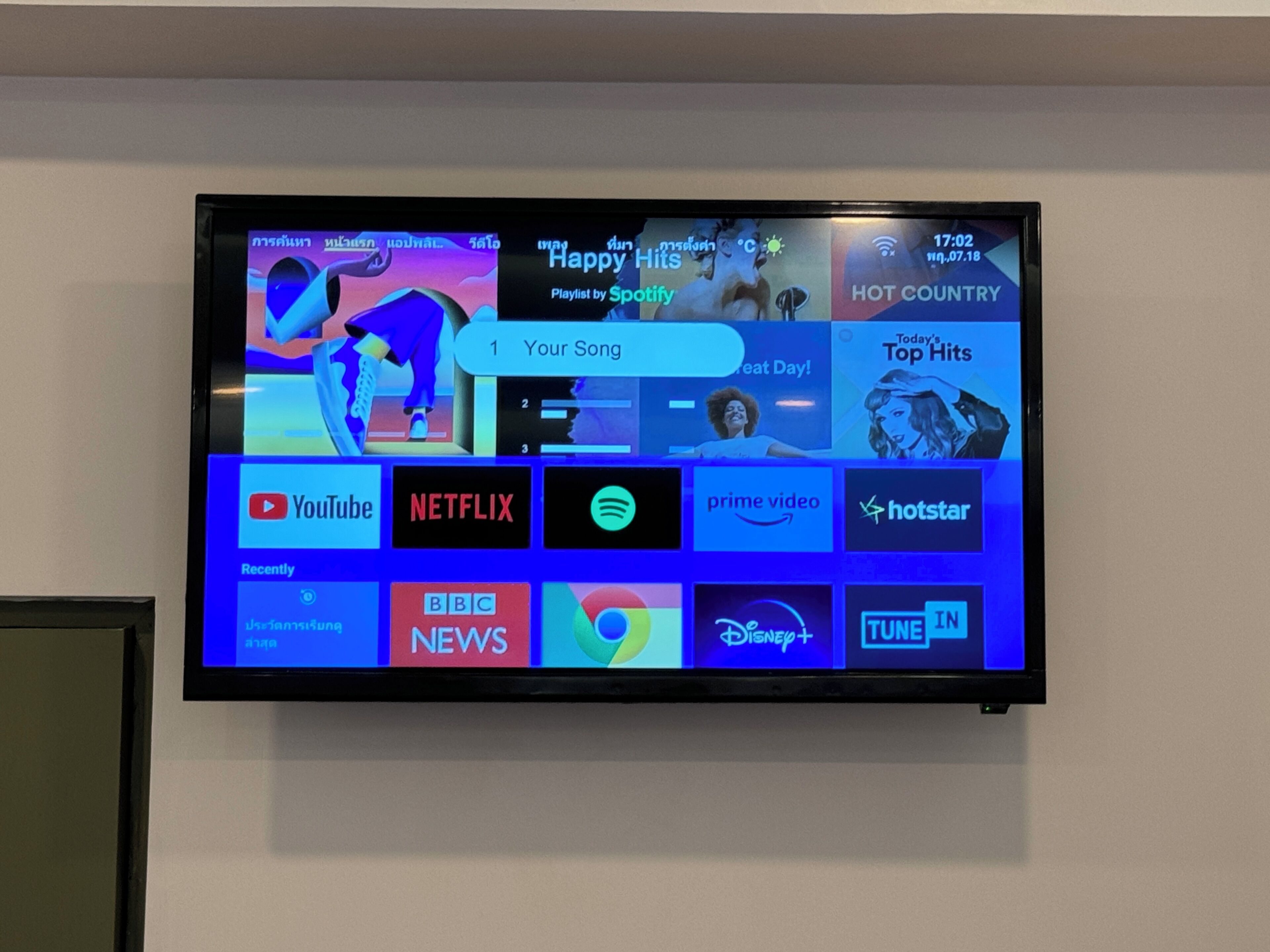 A flat-screen TV mounted on a wall displaying a streaming service interface with various app icons.