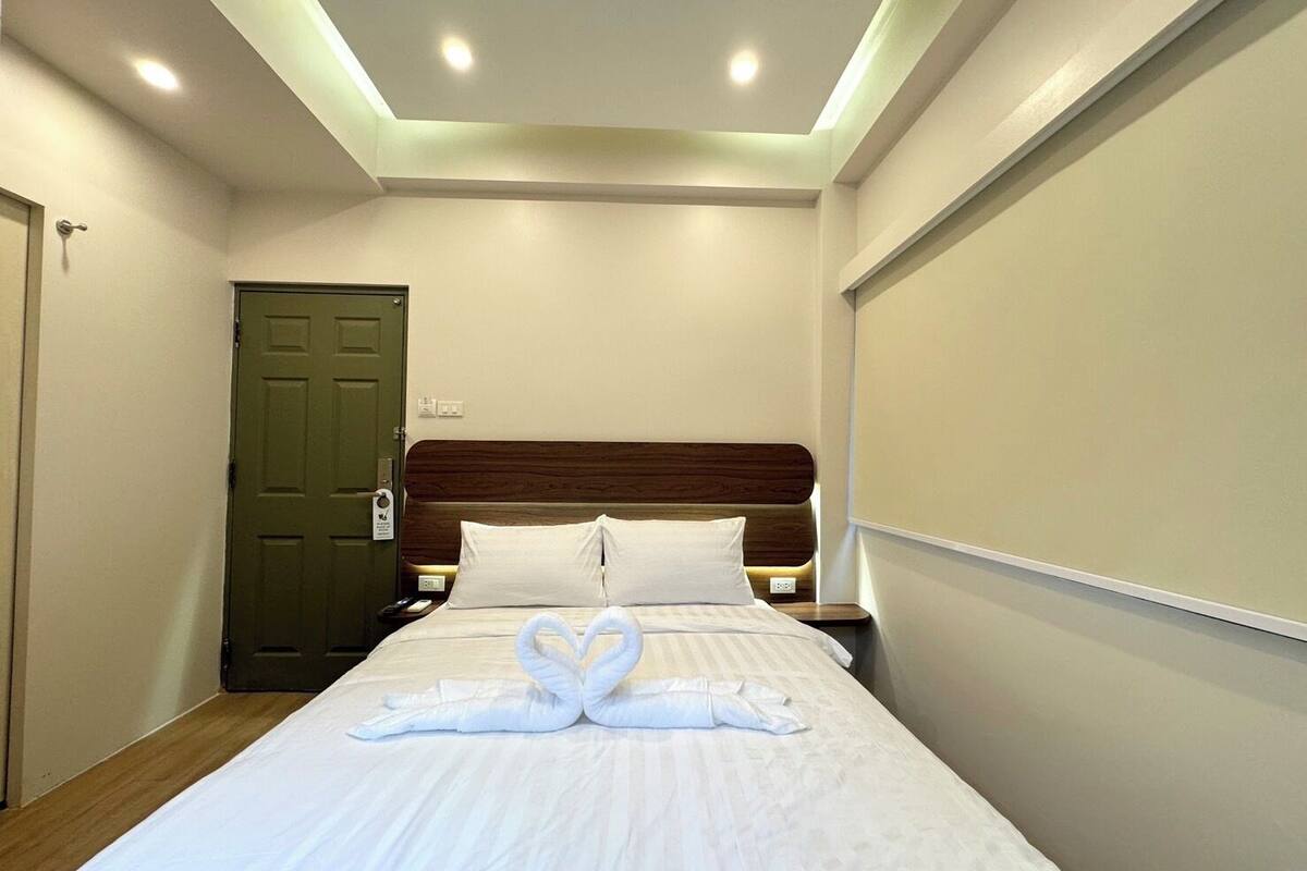 Ein Hotelzimmer mit einem ordentlich bezogenen Bett, einem hölzernen Kopfteil und einer grünen Tür.