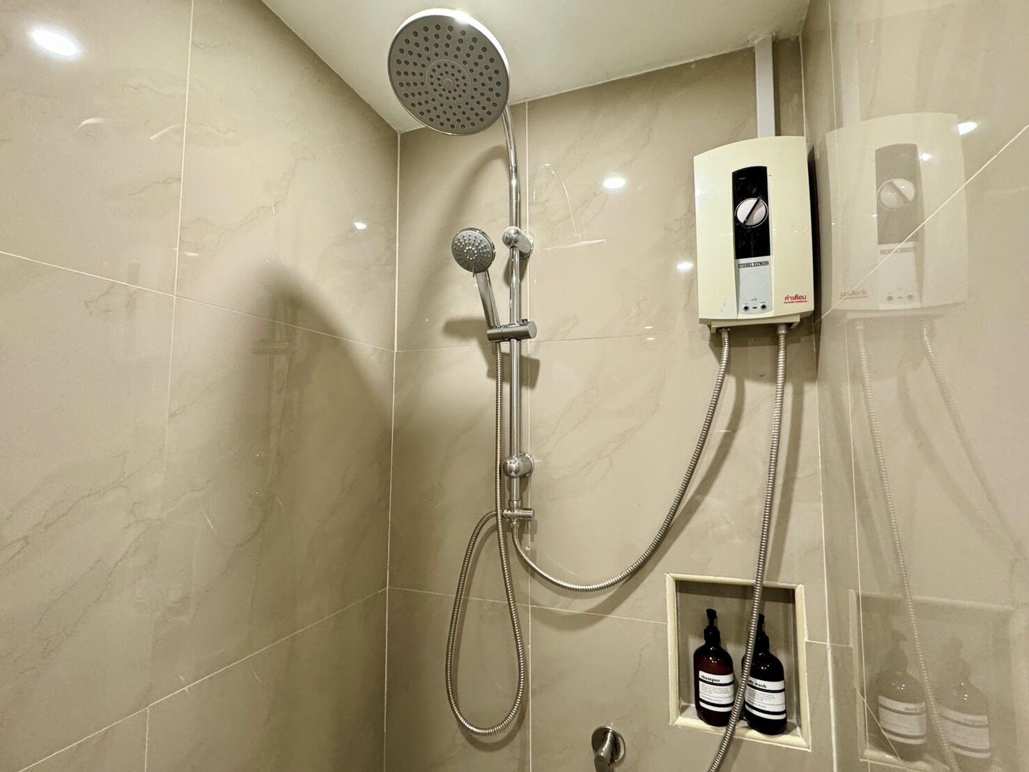 A shower with a handheld showerhead, a wall-mounted control panel, and a bottle of shampoo.