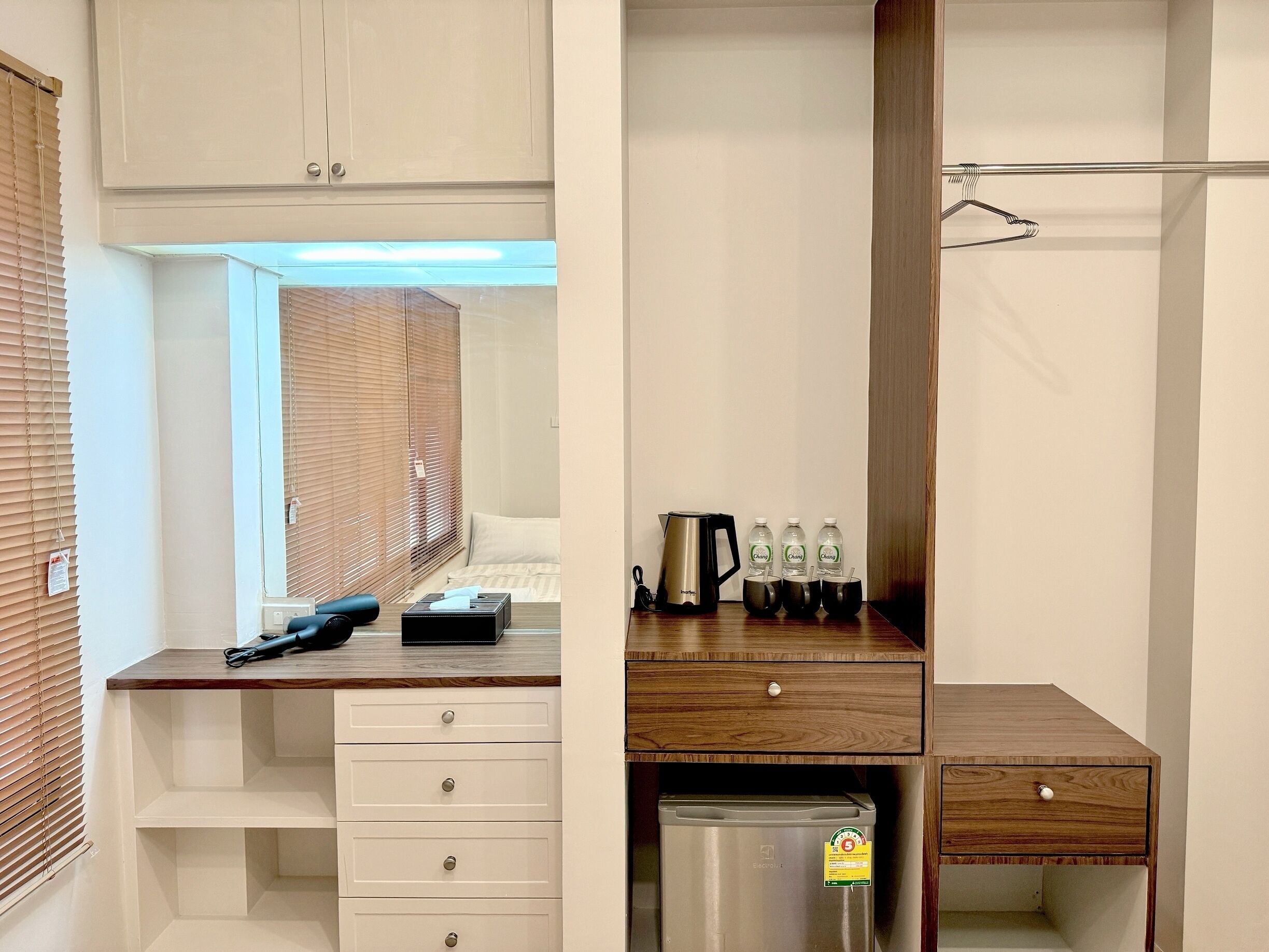 A compact hotel room with a wooden desk, a small refrigerator, and a bed with a window.