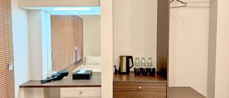 A compact hotel room with a wooden desk, a small refrigerator, and a bed with a window.