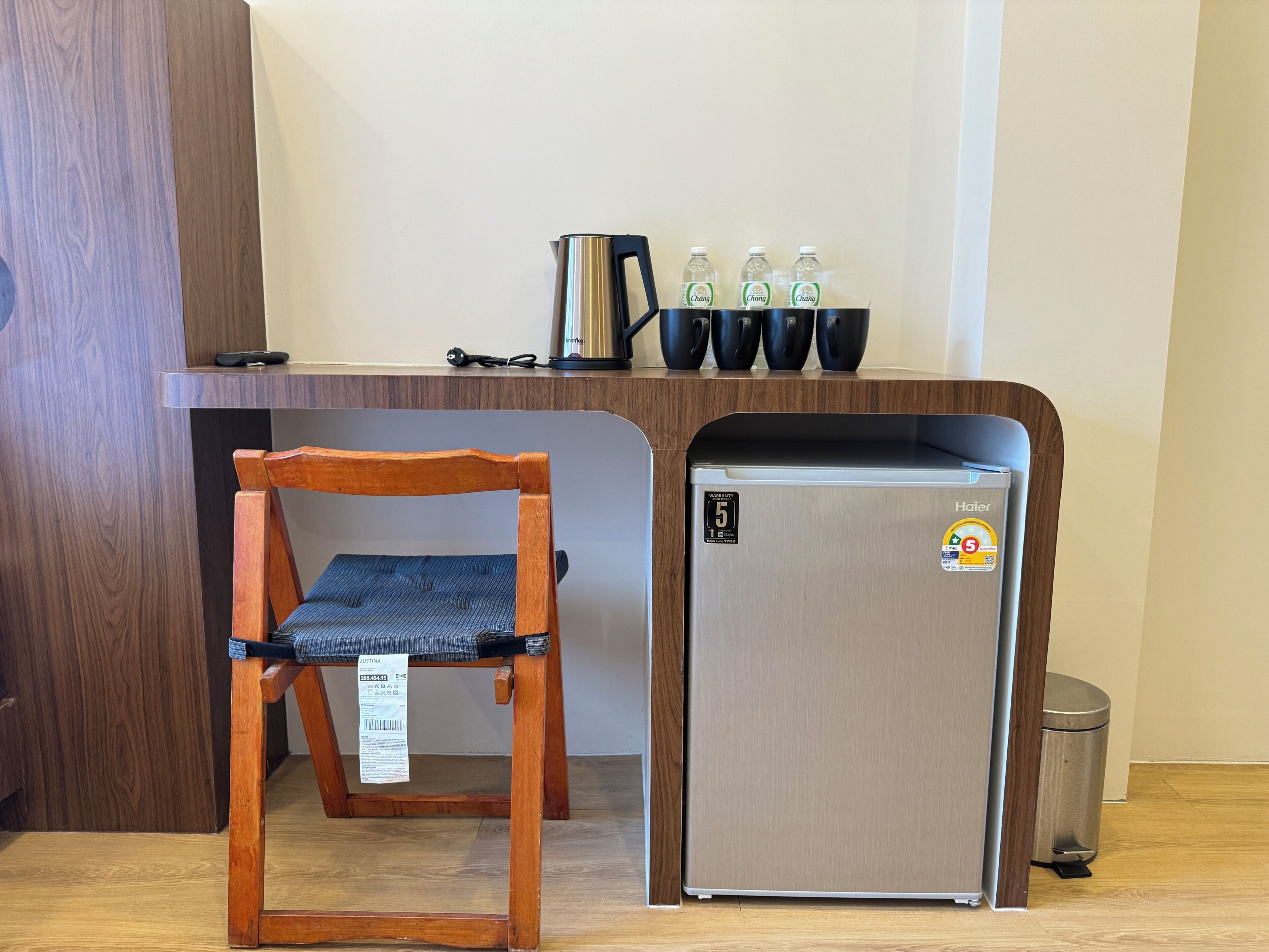 A compact kitchenette with a stainless steel refrigerator, a wooden chair, and a coffee maker on the countertop.