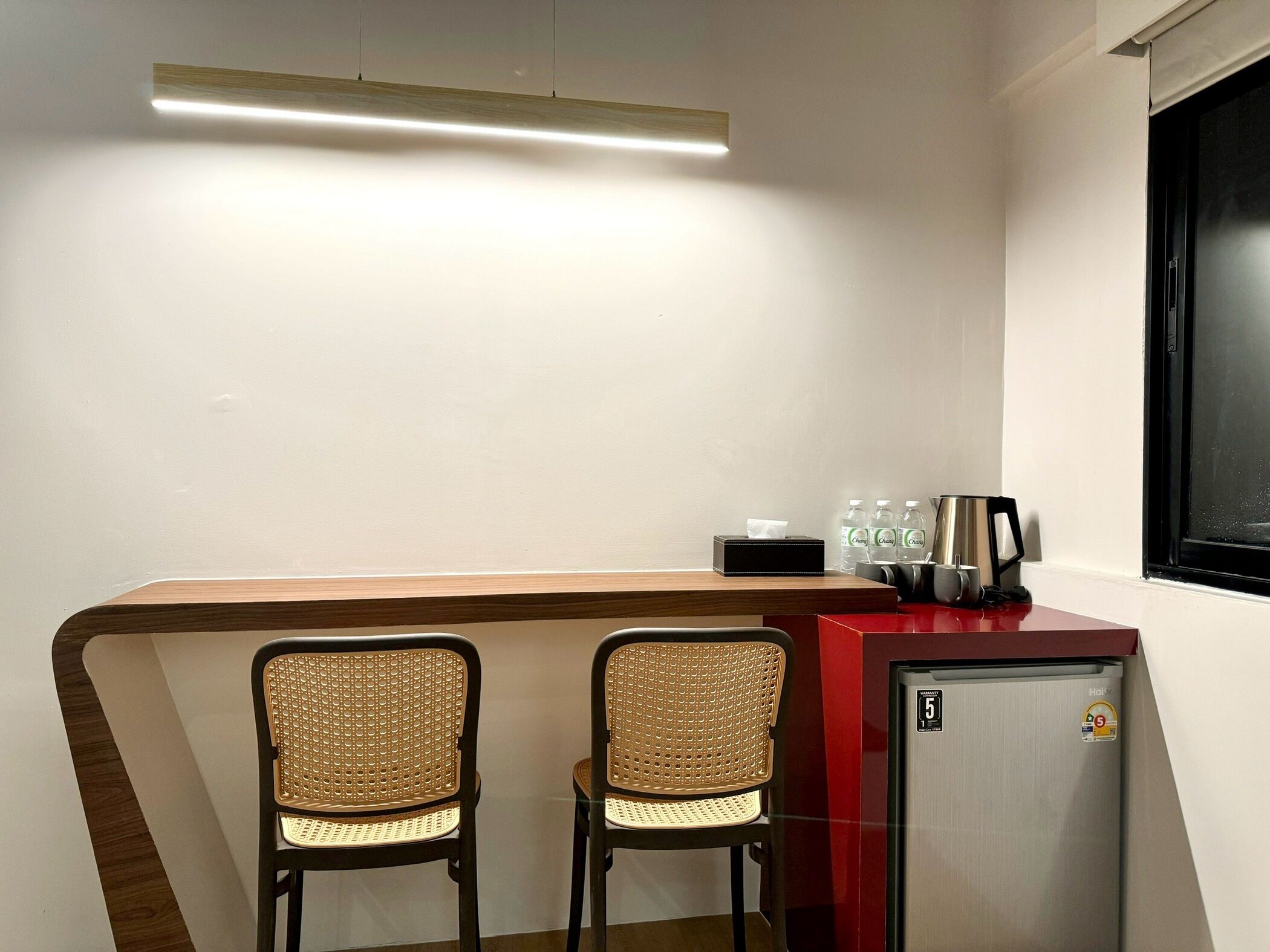 A small kitchenette area with two wicker chairs, a countertop, a refrigerator, and a window.