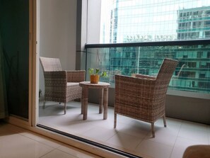 Relax on the balcony with a city view, featuring a wicker chair and small table.
