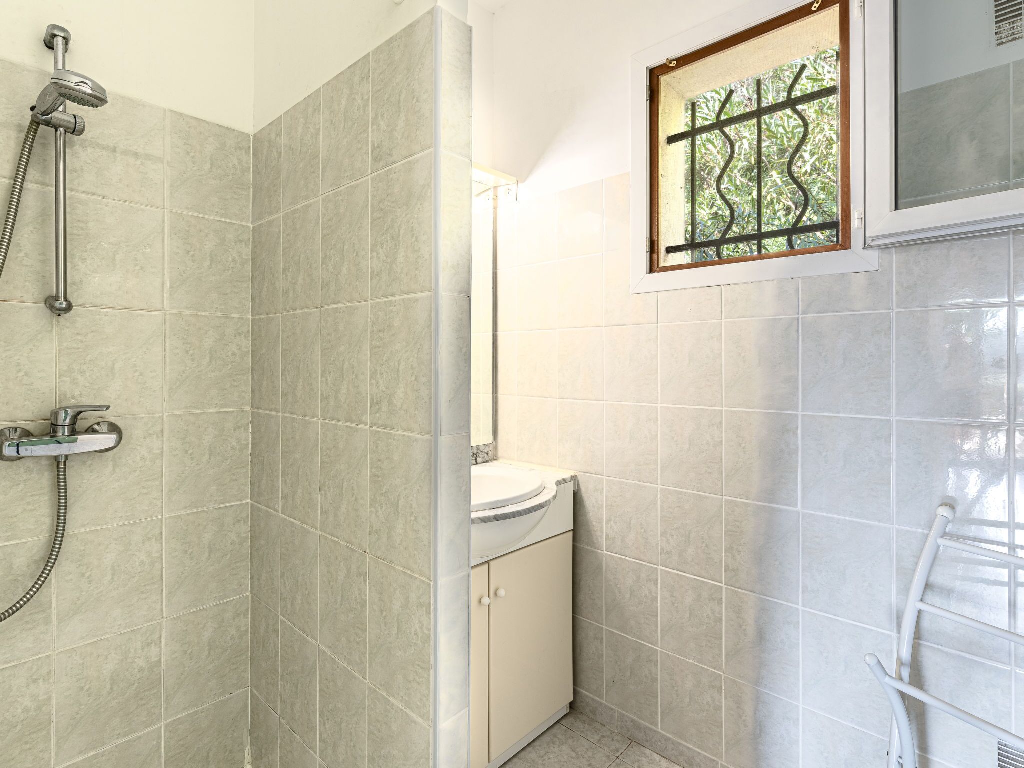 A bathroom with a shower, toilet, and a window with a view of greenery.