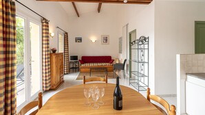 Un comedor con una mesa de madera, cuatro copas de vino y una botella. Se aprecia un sofá rojo y una pequeña mesa con un ordenador portátil al fondo.