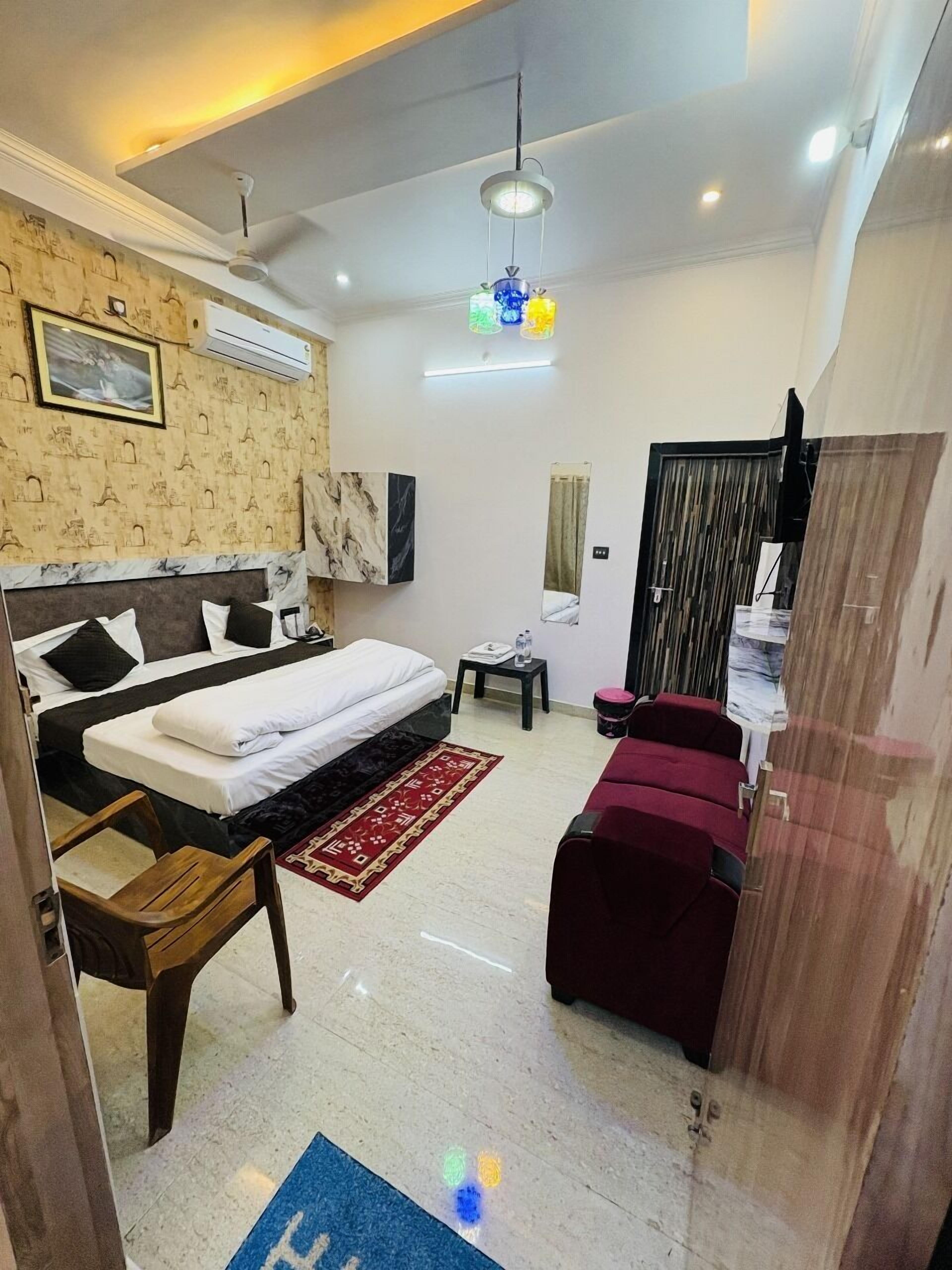 A hotel room with a bed, a desk, a chair, a red sofa, a mirror, and a wardrobe.