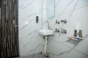 Un baño con lavamanos de mármol blanco, cabina de ducha de vidrio y puerta de madera.
