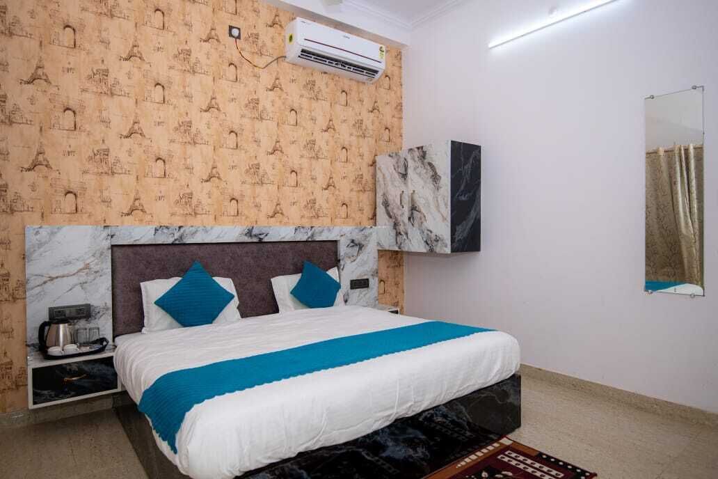 A hotel room with a bed, a marble headboard, a wall-mounted air conditioner, a small table with a kettle, and a patterned wallpaper.