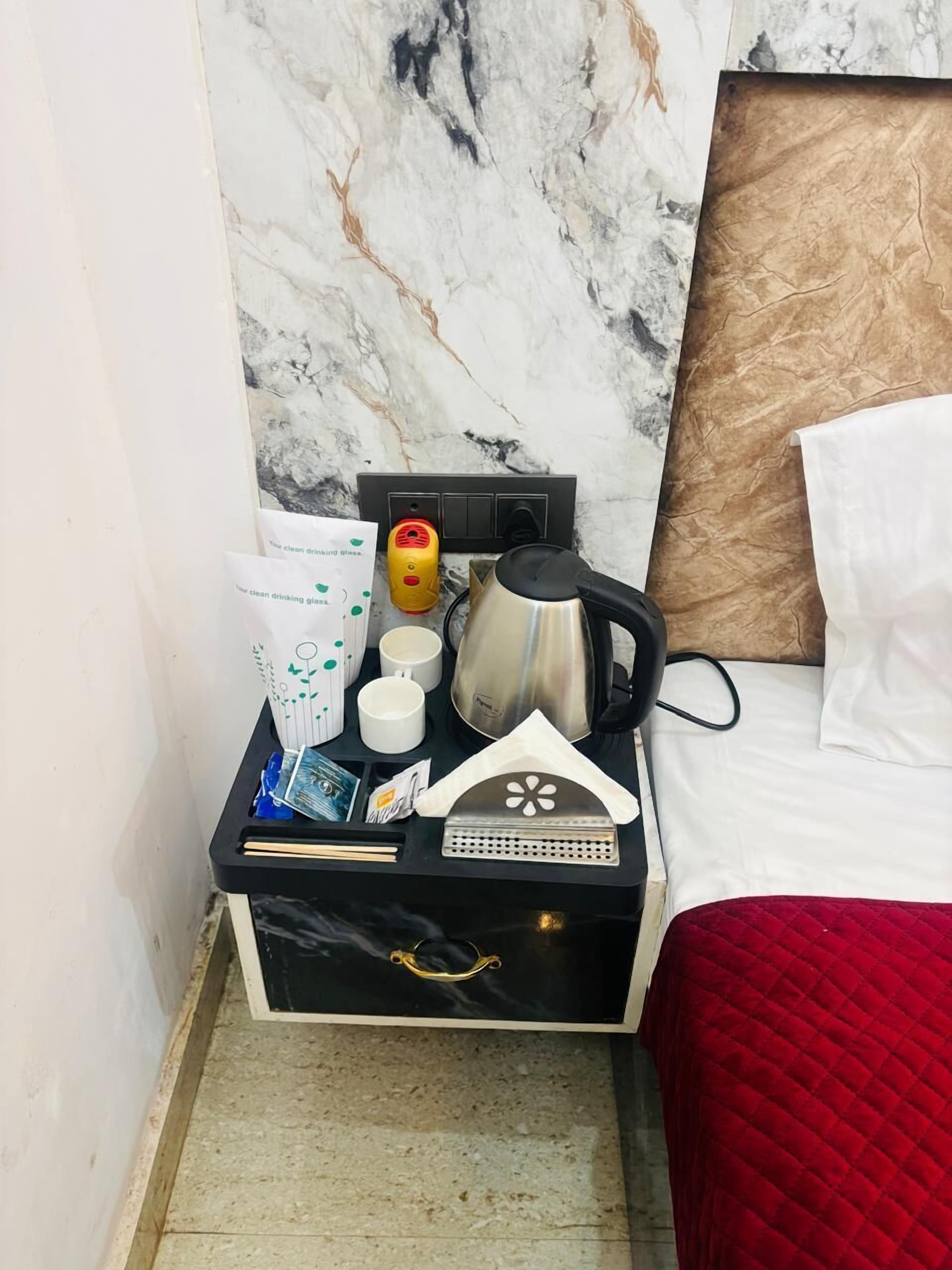 Habitación de hotel impecable con pared de mármol, cama con colcha roja, mesita de noche negra y cafetera.