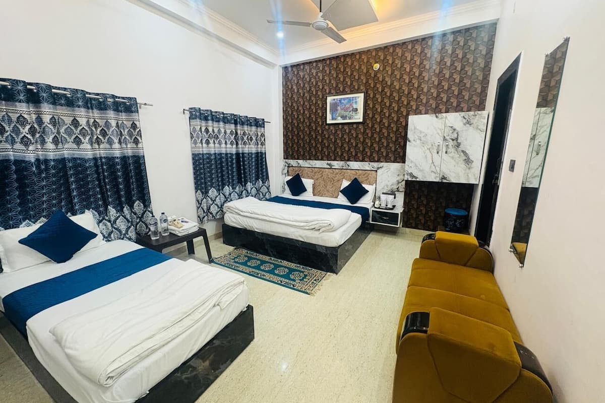A hotel room with two beds, a sofa, a ceiling fan, a marble fireplace, and a wall-mounted TV.
