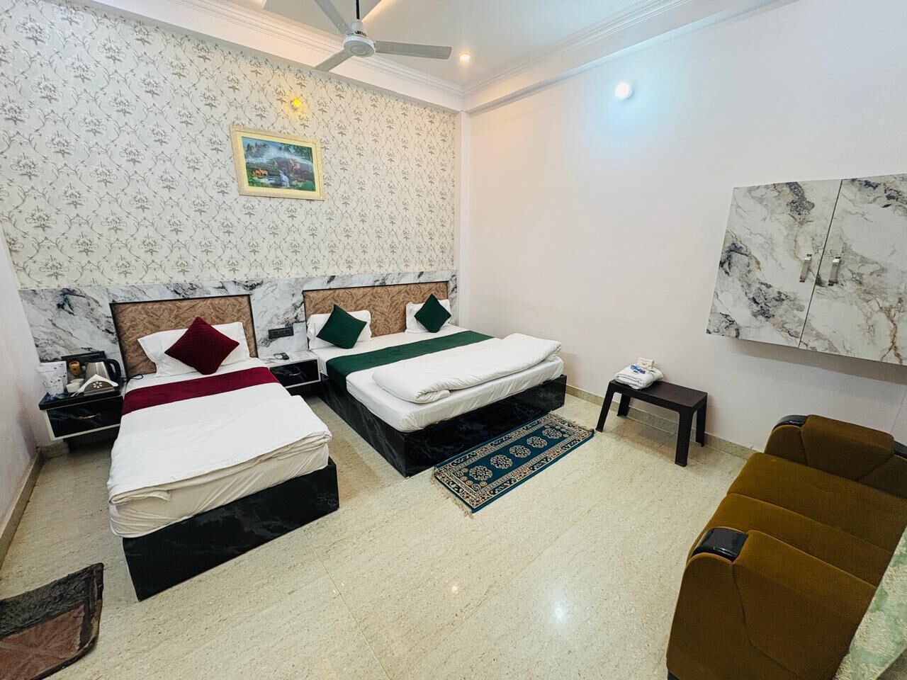 A hotel room with two beds, a ceiling fan, a small table, a sofa, and a marble-patterned wall.