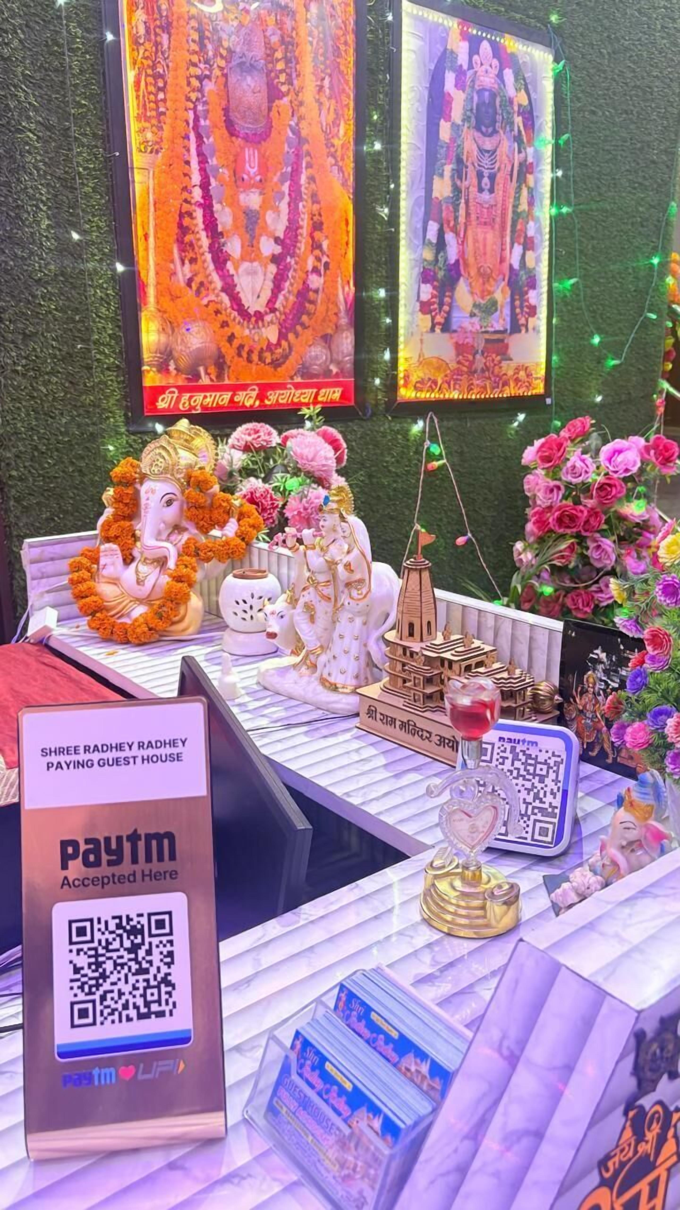 Un santuario con ídolos, un código QR de Paytm y un cartel para Shree Radhey Radhey Paying Guest House.