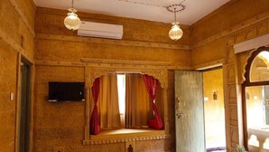 A room with a traditional design, featuring a built-in window with curtains, a flat-screen TV mounted on the wall, and an air conditioning unit. - Hotel Garh Meera (Jaisalmer)