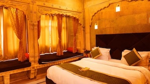 A hotel room with a large bed, a bench, and curtains. - Hotel Garh Meera (Jaisalmer)