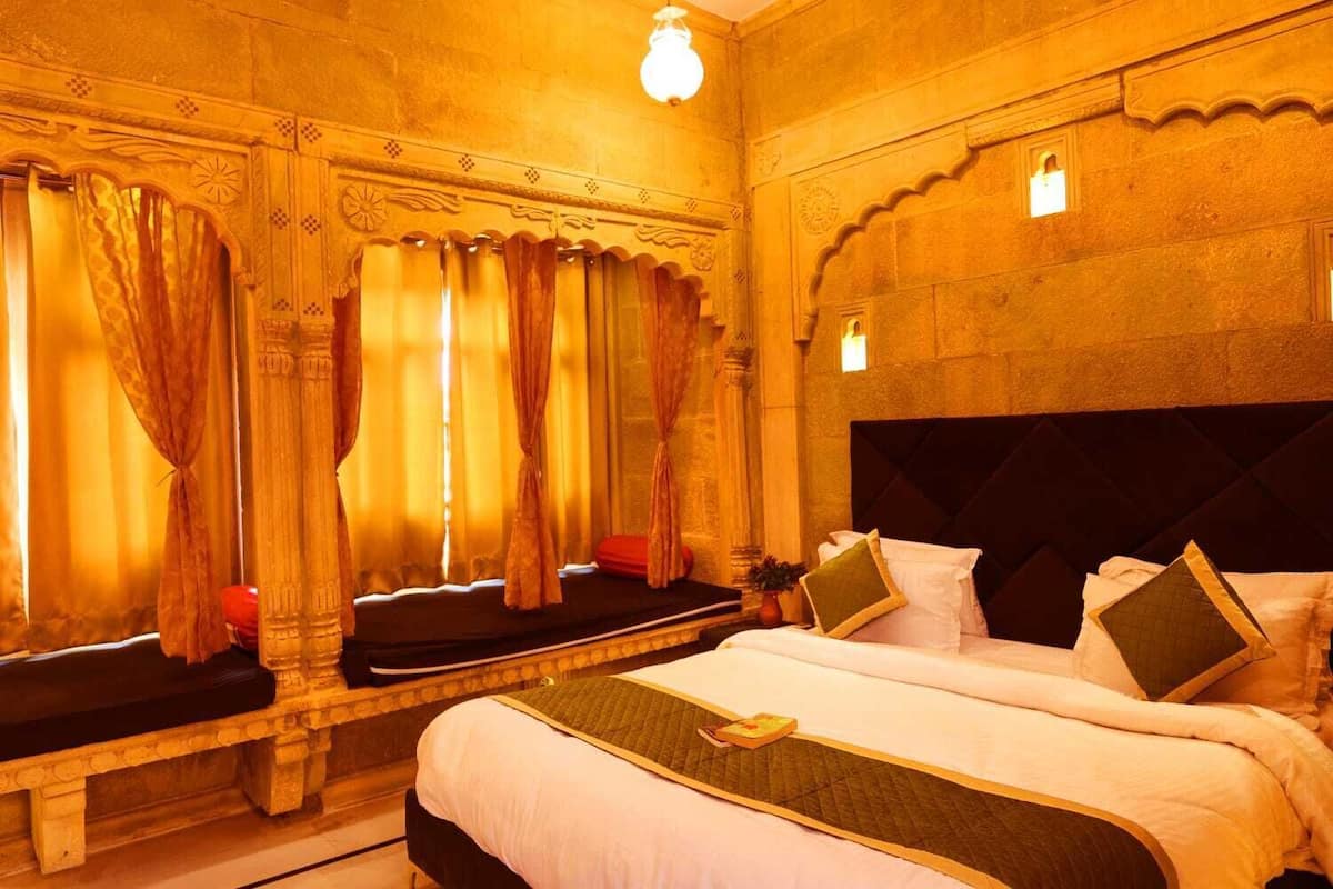 A hotel room with a large bed, a bench, and curtains.