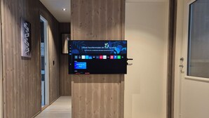 Una habitación de hotel moderna con televisor montado, piso de madera y una pequeña mesa decorativa con objetos esféricos.