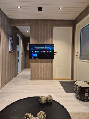 A modern hotel room with a mounted TV, a wooden floor, and a small decorative table with spherical objects.