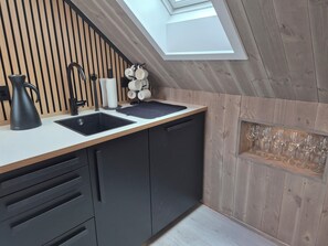 A modern kitchen with a wooden wall, a black sink, a kettle, and a wine rack.