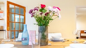 A dining table set with white plates, bowls, cutlery, and a vase with flowers. - Porthilly by Interhome (Mevagissey)