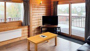 A log cabin room with a wooden table, a television, and a sofa. - 1 bedroom accommodation in Greetham (Greetham)