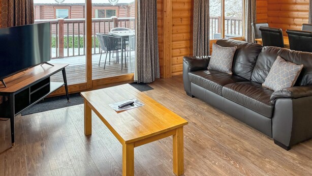 A cozy cabin interior with a wooden floor, a leather sofa, a TV, and a balcony with a table and chairs. - 1 bedroom accommodation in Greetham (Greetham)
