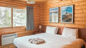 A wooden cabin bedroom with a bed, a nightstand, a lamp, a radiator, and two framed pictures on the wall. - 1 bedroom accommodation in Greetham (Greetham)