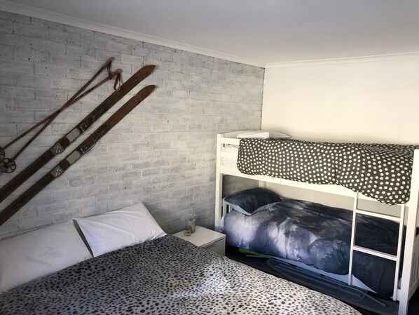 A bunk bed with a polka dot blanket, a leopard print bedspread, and a white pillow. There are skis leaning against the wall and a small bedside table with a bottle. - Perfect Located Apartment in the Heart of Hotham (Hotham Heights)