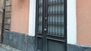 Een zwart metalen hekwerk met decoratieve patronen, bevestigd aan een gebouw met een perzikkleurige muur en witte sierlijsten.