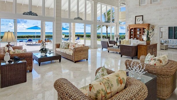 A spacious living area with wicker furniture, large windows offering ocean views, and a ceiling fan. - Ocean Mist Villa - by ZenBreak (Belair)