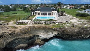 A large house with a swimming pool, located on a rocky coastline with a view of the ocean. - Ocean Mist Villa - by ZenBreak (Belair)