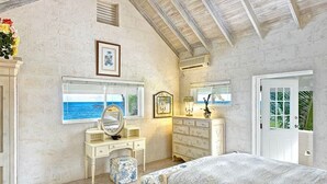 A bedroom with a large bed, a vanity with a mirror, a dresser, and a window with a view of the ocean. - Ocean Mist Villa - by ZenBreak (Belair)