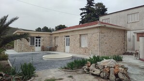 A stone house with a tiled roof, a small garden with plants and rocks, and a circular outdoor seating area. - Villa Phyllia, a Property With History (Heraklion)