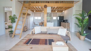 A spacious living area with a loft bedroom, a wooden staircase, and a kitchen in the background. - Guest House Terrace (Miyakojima)