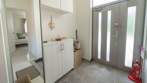 A clean, modern hallway with a white cabinet, a wicker basket, and a fire extinguisher near a sliding door. - Guest House Terrace (Miyakojima)