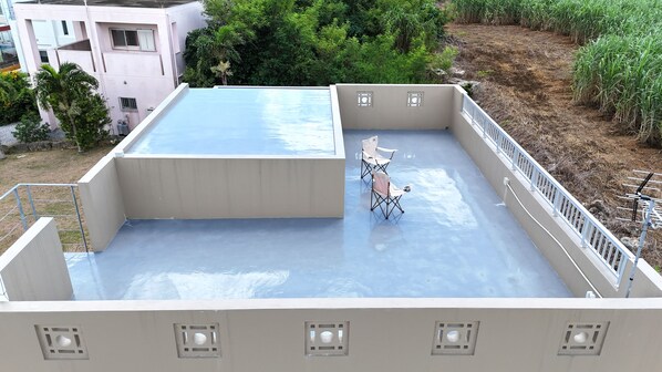 Una terraza en la azotea con superficie plana, dos sillas plegables y una pequeña estructura blanca.